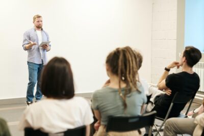 A man stands in front of a row of people, giving a presentation. By Fauxels on Pexels