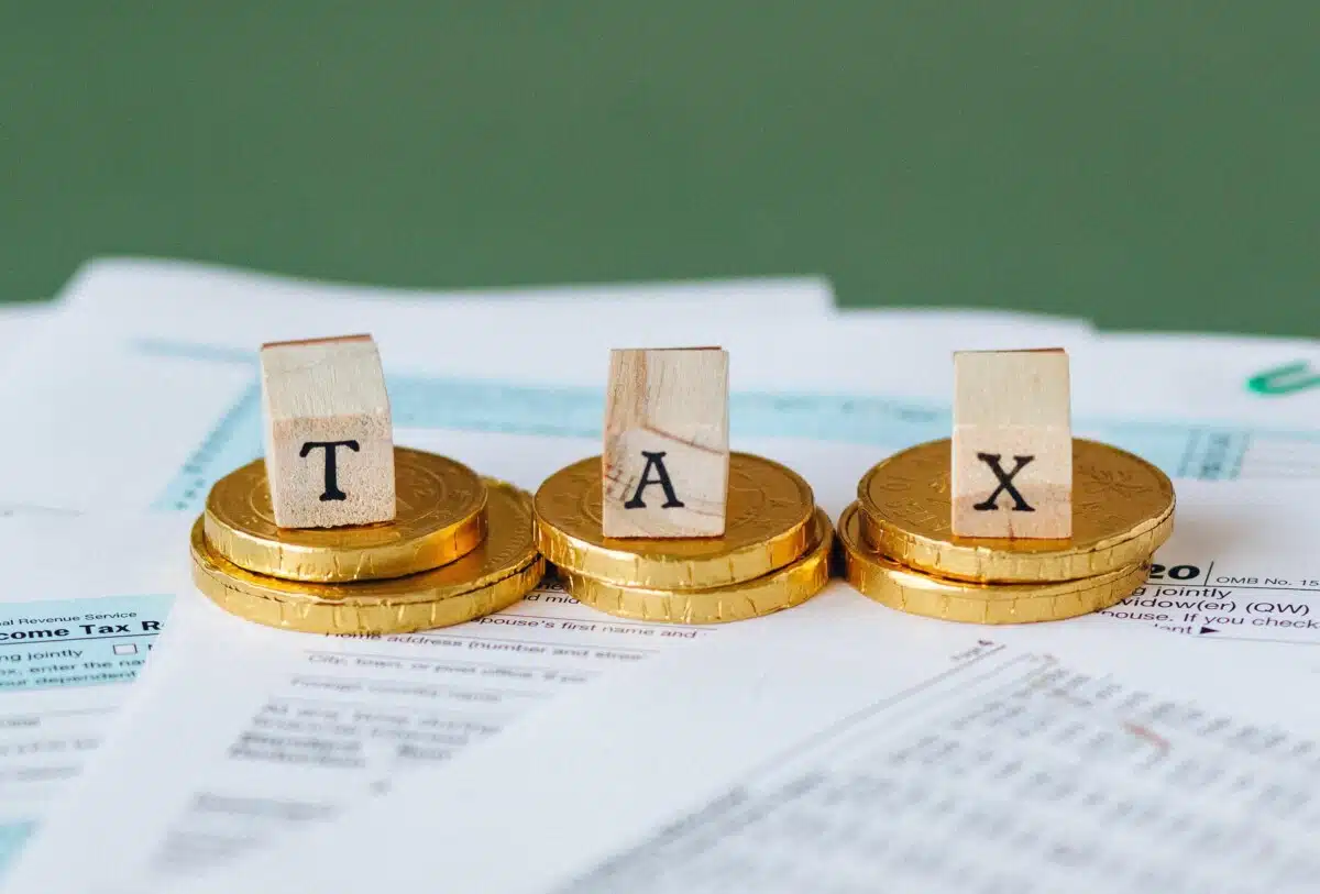 Wooden blocks spelling out tax sit on top of gold coins. By Nataliya Vaitkevich on Pexels