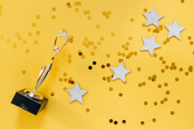 An award statuette and gold stars against a yellow background. By Nataliya Vaitkevich on Pexels