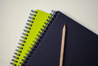 Two ringbound notepads, one lime green and one black, with a pencil. By tookapic on pixabay