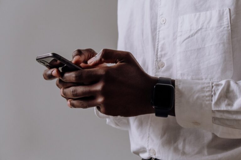 A black man in a white shirt holds his phone. By Cottonbro on Pexels