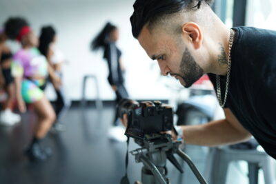 A man looks down at a camera as he films a dance class. From Together TV's Diverse Film Fund. Credit: Blaise Singh.