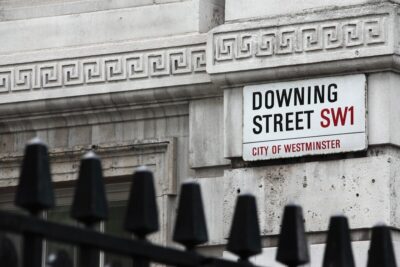 A street sign reading Downing Street SW1 on a stone building, behind a black metal fence. By Public Domain Pictures on Pixabay