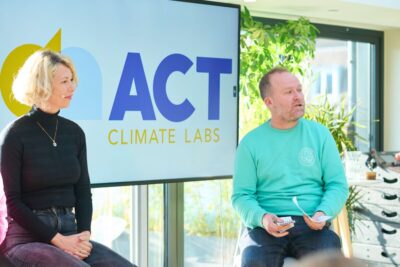 Harriet Kingaby (Head of ACT Climate Labs), Jake Dubbins, Managing Director of Media Bounty sitting at the front of an event, in front of a screen with ACT on it.