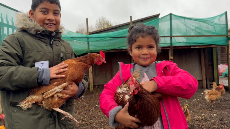 2 children smile as they hold chickens. A project funded by the National Lotery Community Fund