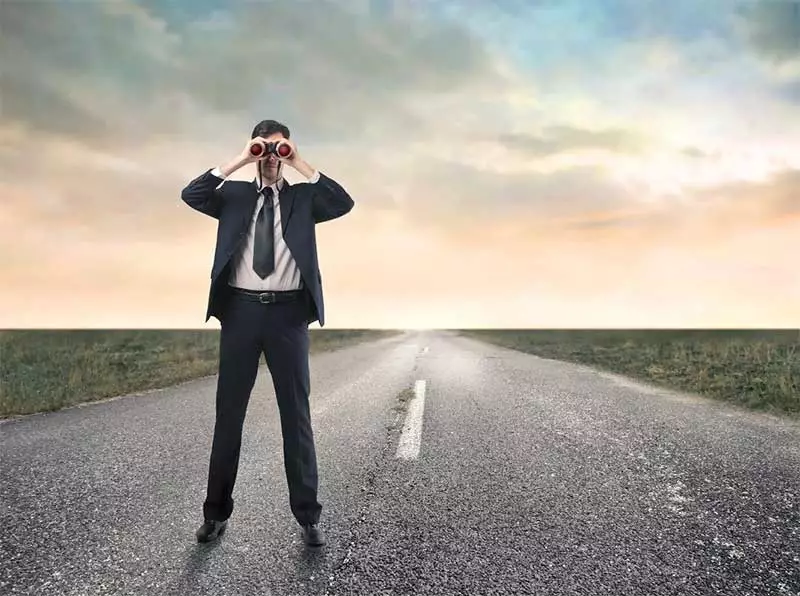 Man standing on an empty road looking ahead through binoculars. Photo: Giles Pegram-purchased image.