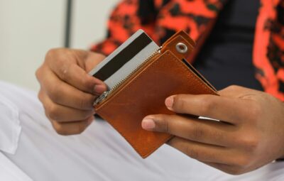 A man's hands pull a payment card out of a brown wallet. By Cup of Couple on Pexels