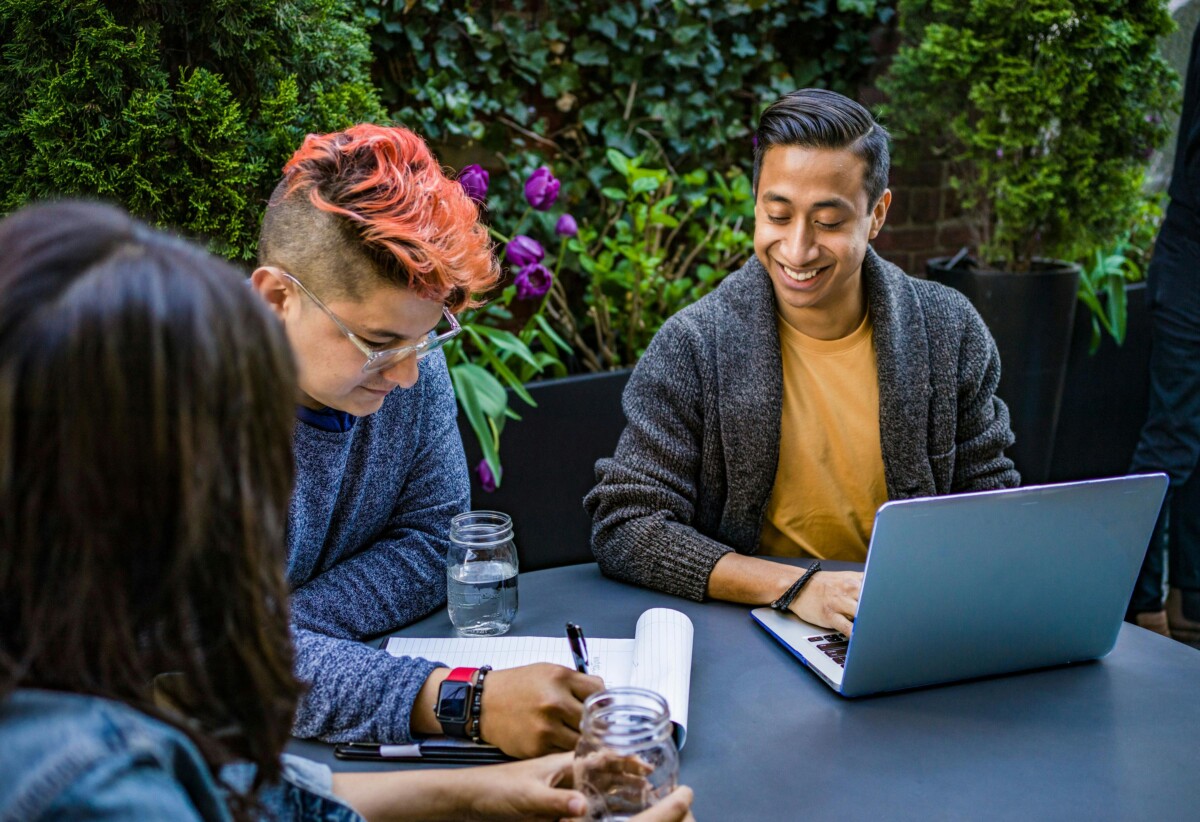 3 diverse young people sit at a table in the outdoors. By Jopwell on pexels