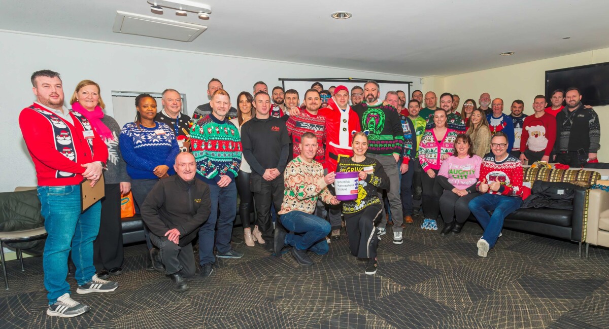 SBH Scotland members gather, wearing Christmas jumpers. At the front two kneel holding a charity collection bucket