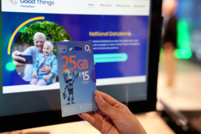A hand holds up a Virgin Media O2 data card in front of a computer screen that says National Databank