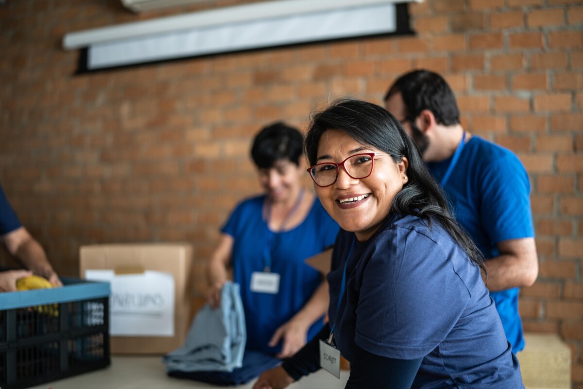 Woman with glasses smiles at the camera while working with colleagues at a charity clothing scheme.