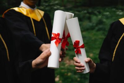Graduates holding their certificates, tied with red ribbon. By George Pak on pexels