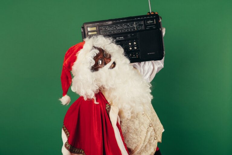 A black Father Christmas holds a radio on his shoulder, listening to music. By Koolshooters on Pexels