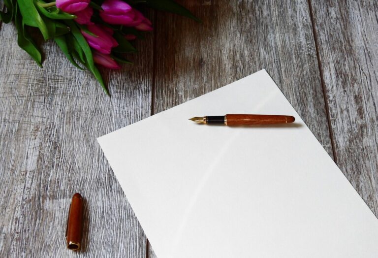 a fountain pen lies on a sheet of paper, on a wooden table with a bunch of fuschia tulips