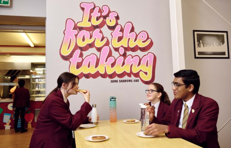 Pupils eating in a school cafeteria with the phrase It's for the taking painted on the wall as part of the Amazon and Prince's Trust partnership