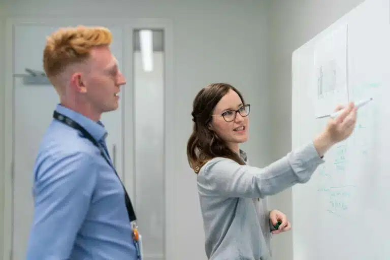A man looks at a whiteboard where a woman is presenting research. By This is Engineering on pexels