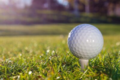 A golf ball in close up on a grassy course with soft evening summer light, and a background of tree. By Kindel Media on Pexels