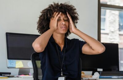 A woman turns from her computer and puts her hands to her head in an expression of stress. By Mizuno K on Pexels