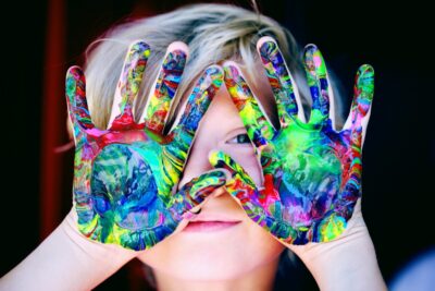 A young child peeks out behind painted hands. By Alexander Grey on Pexels