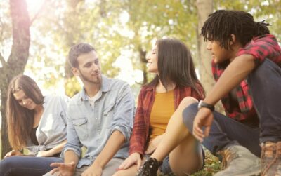 A group of 4 multi-ethnic young people sit chatting under some trees. By Andrea Piacquadio on Pexels
