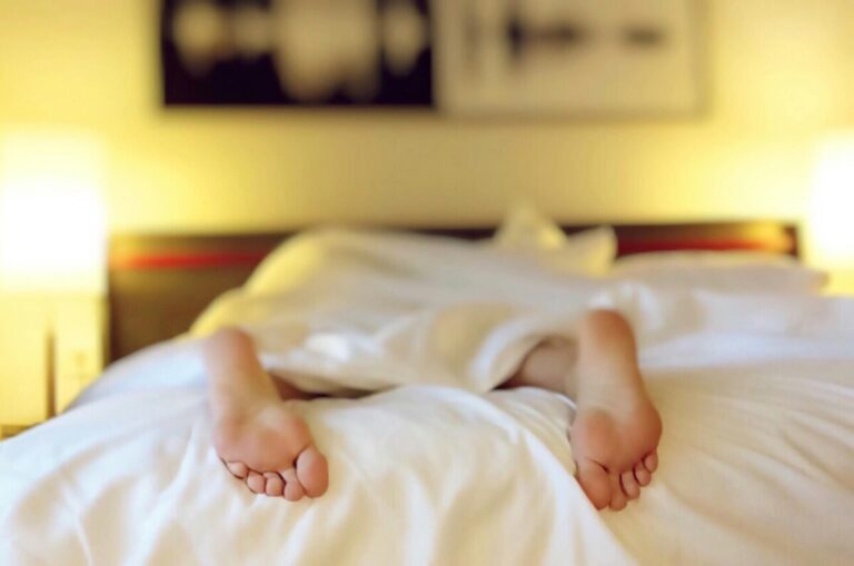 a view of a person's feet poking out from under a duvet as they lie face down in bed. By Pixabay on pexels
