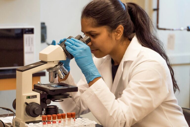 A female scientist looks at samples under a microscope. By Trust 