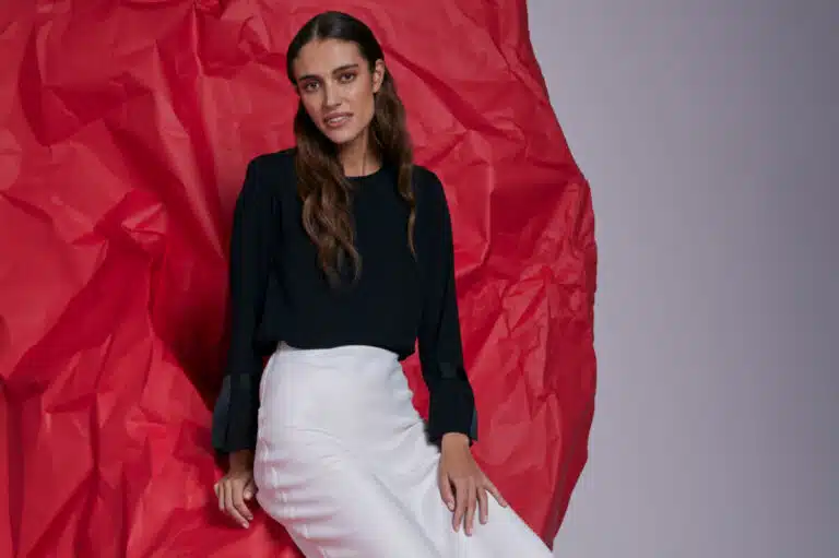 A woman in a black shirt and white skirt sits against a red background as part of Salvation Army's Take Back Scheme fashion campaign, encouraging people to donate more unwanted clothing