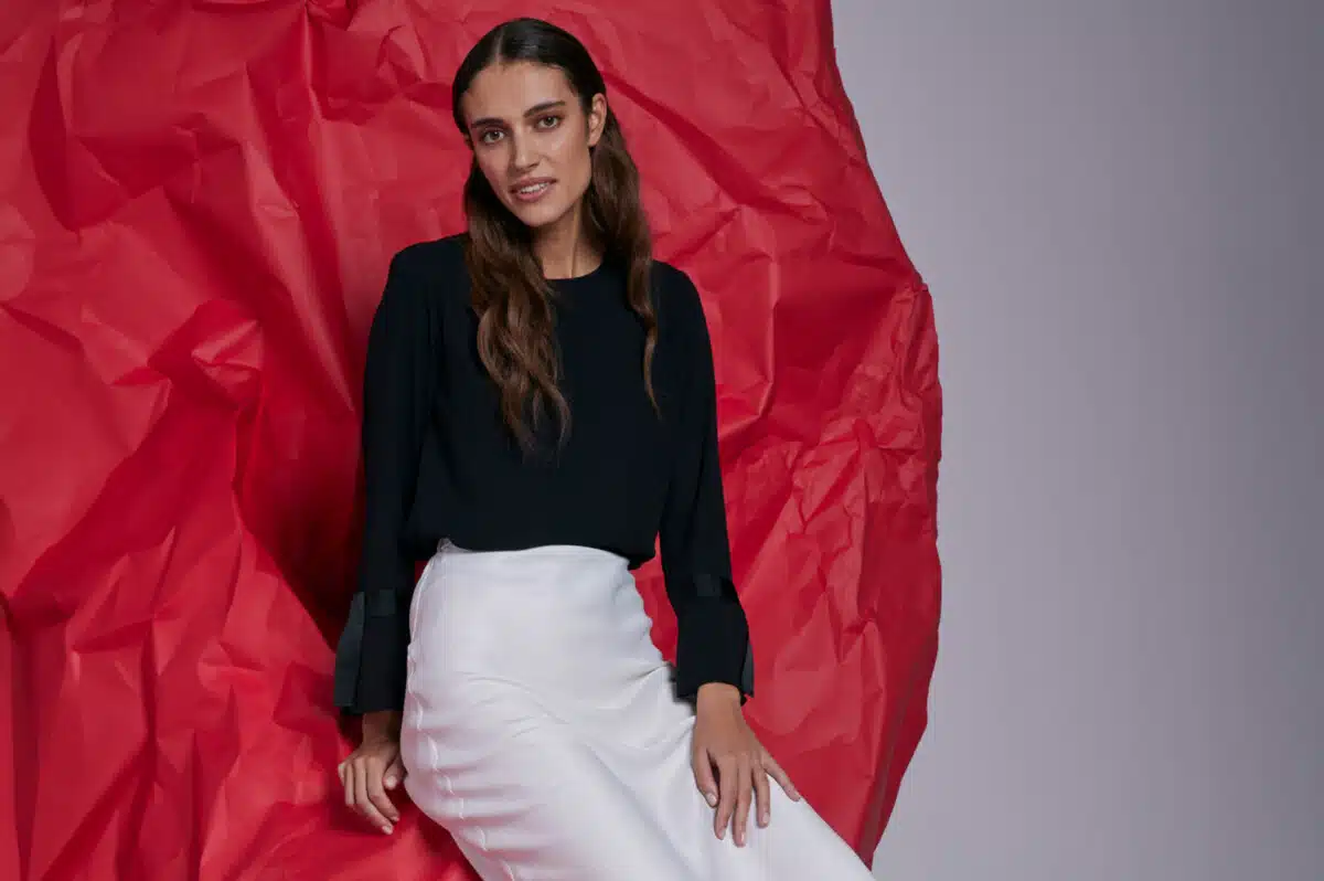 A woman in a black shirt and white skirt sits against a red background as part of Salvation Army's Take Back Scheme fashion campaign, encouraging people to donate more unwanted clothing