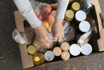 A close up of a hand putting food into a box at a food bank