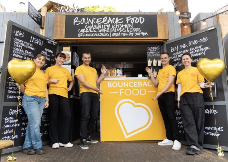 A group of people dressed in yellow t-shirts stand in front of their food stall called Bounceback Food.