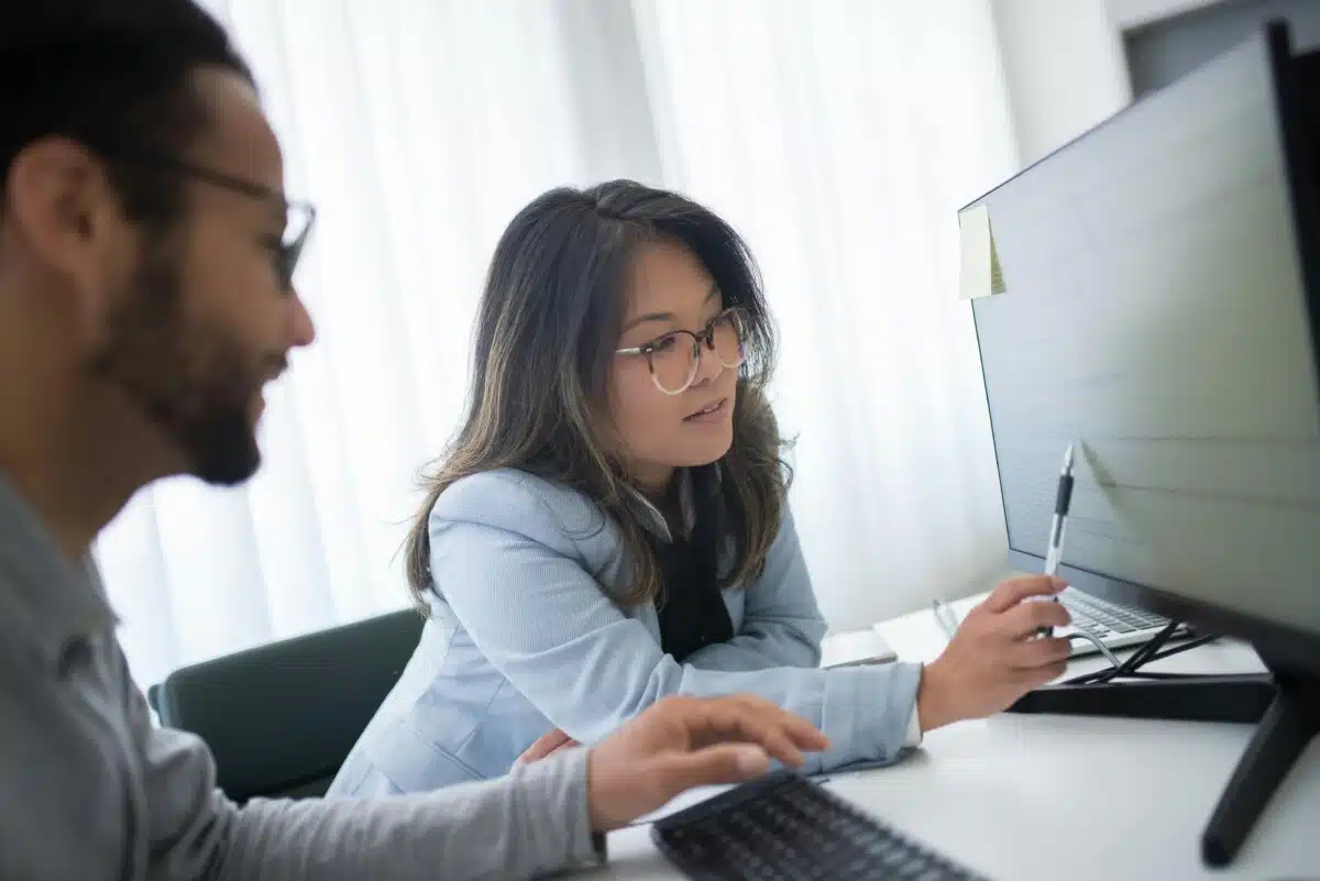 Two people in an office look at something on a computer screen. By Kampus Production on Pexels