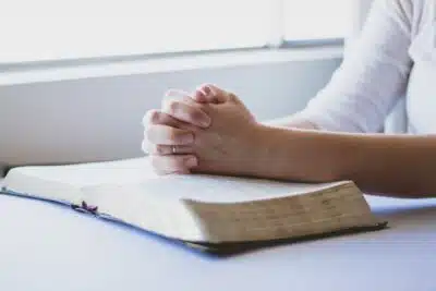 A woman's hands in prayer on a Bible. By Reenablack on Pixabay.