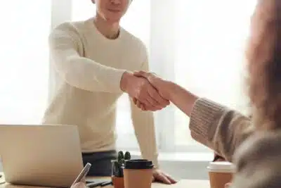 Two people shaking hands over a desk at an interview.