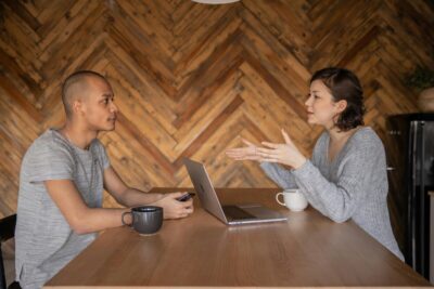 A man looks at a woman as she talks to him across a desk. By KATRIN BOLOVTSOVA on pexels