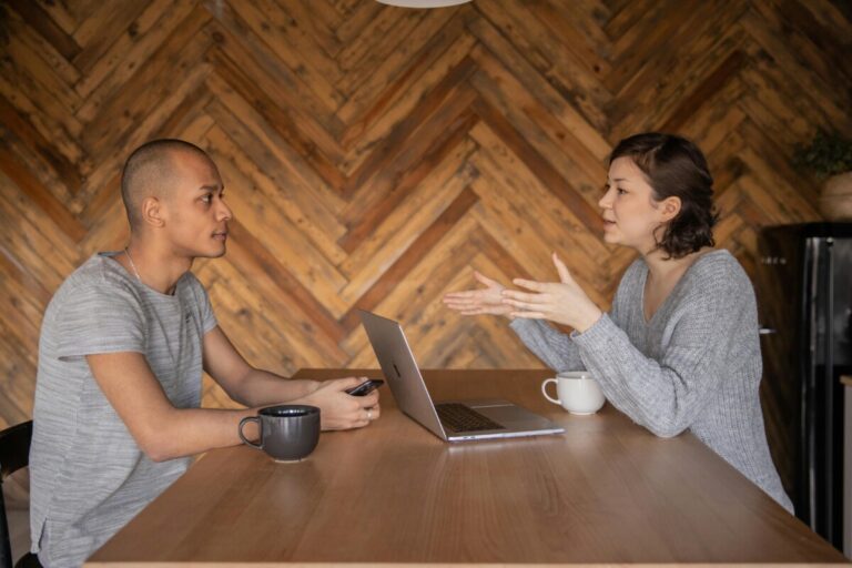 A man looks at a woman as she talks to him across a desk. By KATRIN BOLOVTSOVA on pexels