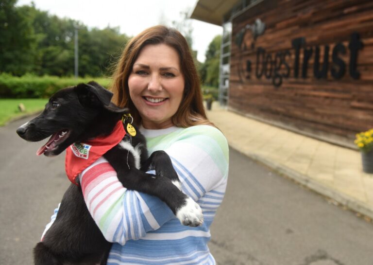 A woman smiles at the camera as she cuddles a dog at a Dogs Trust home