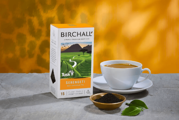 A box of Birchall Serengeti tea next to a cup of tea, and a small dish of tea leaves