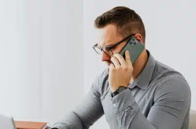 A man in glasses and grey shirt on a phone. By Karolina Grabowska on Pexels