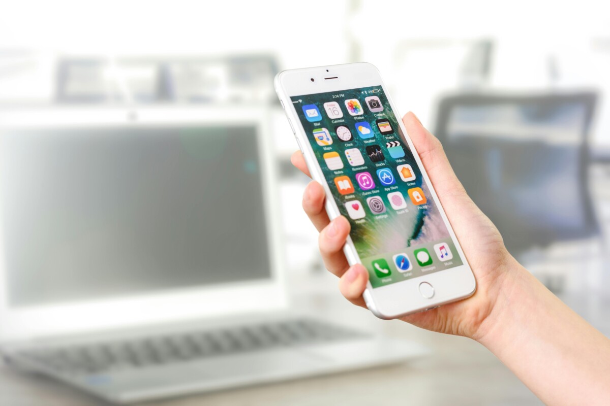 A hand holds a phone in front of a laptop. By asphotography on pexels.