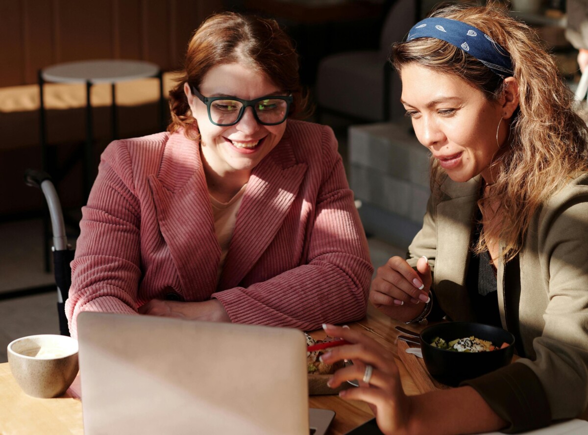 Two women smile as they watch something on a laptop screen. By marcus aurelius on pexels