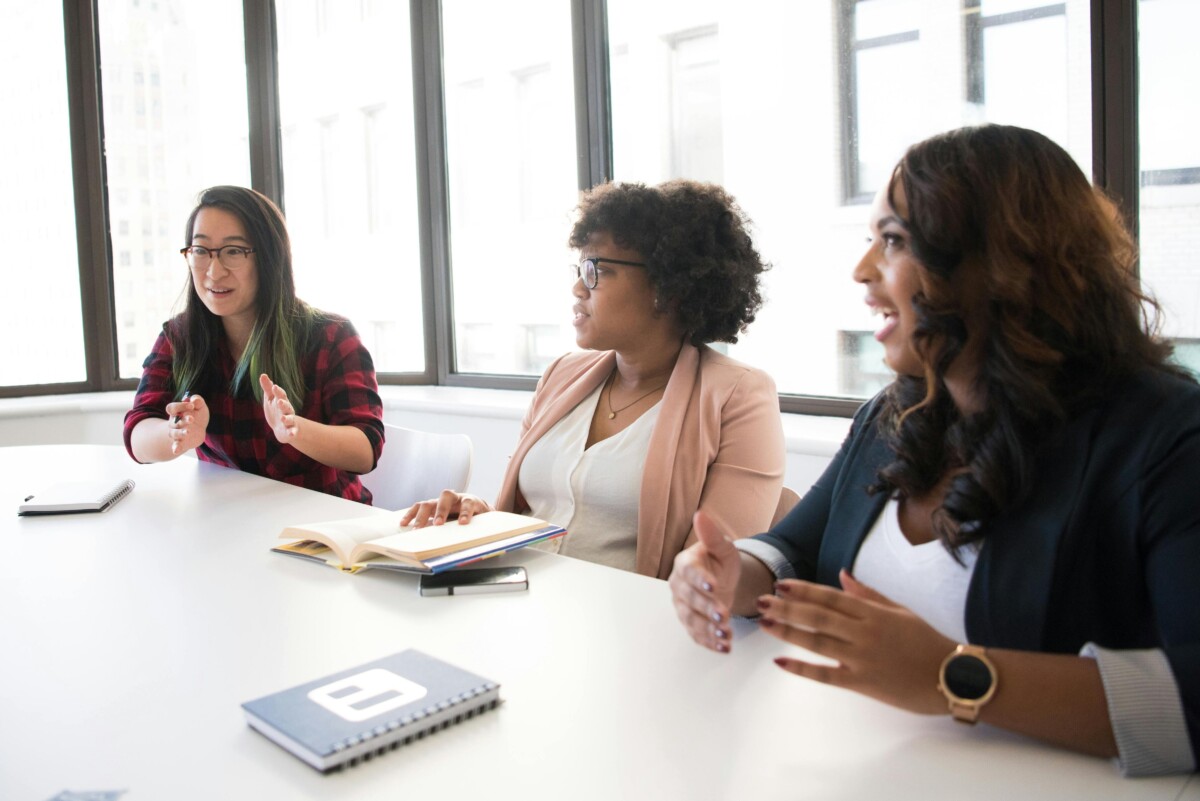 Three women in discussion, seated around an office table. By Christina Morillo on Pexels