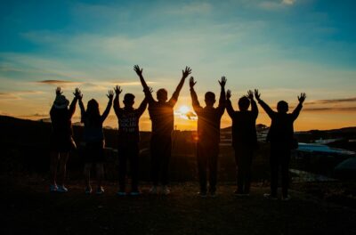 Young people with their hands in the air, silhouetted against a sunset. By Min An on Pexels