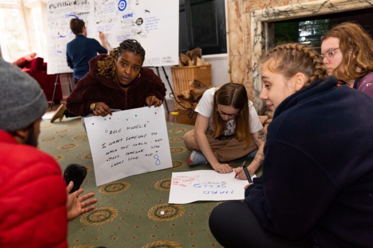 A small group of young people sit on the floor in a circle, taking part in a workshop with UK Youth,