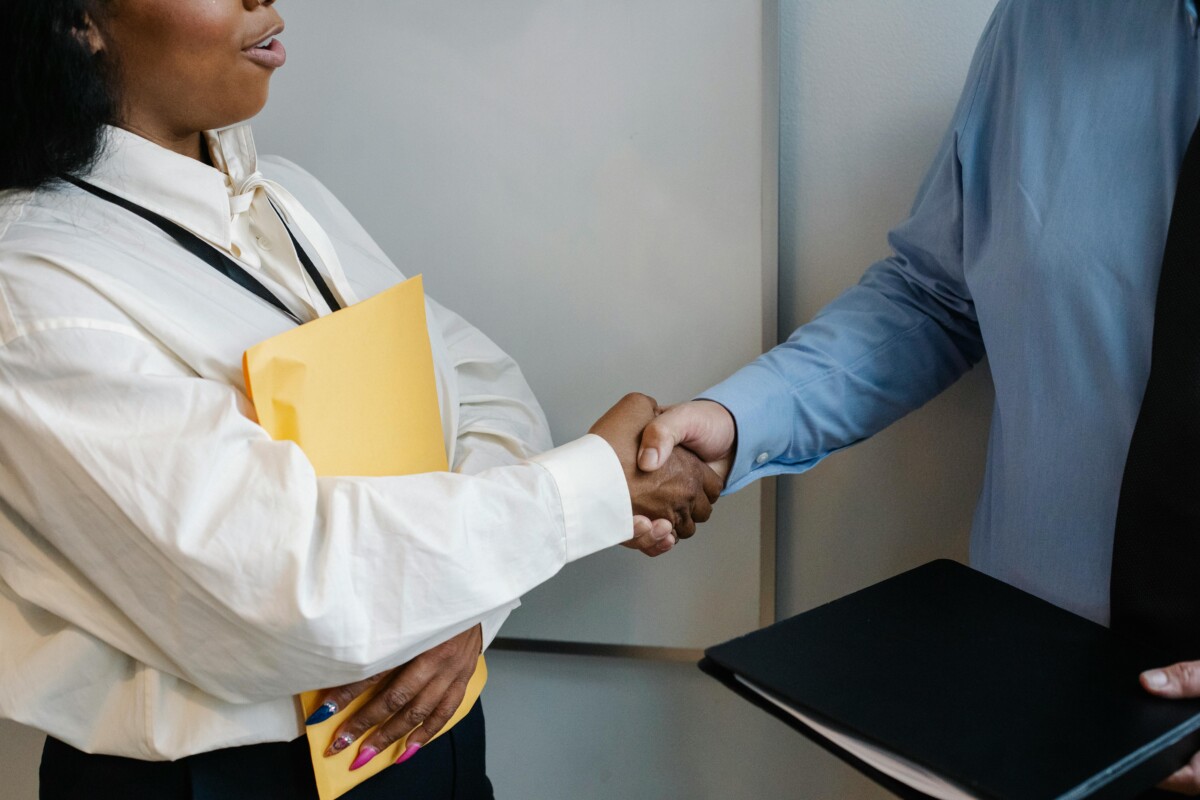 Two people - one holding a folder and the other a brown file, shake hands. By Sora Shimazaki on Pexels