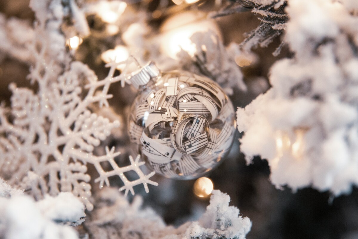 A bauble filled with pieces of paper showing musical notes, on a white Christmas tree. By Ryan Johns on Unsplash