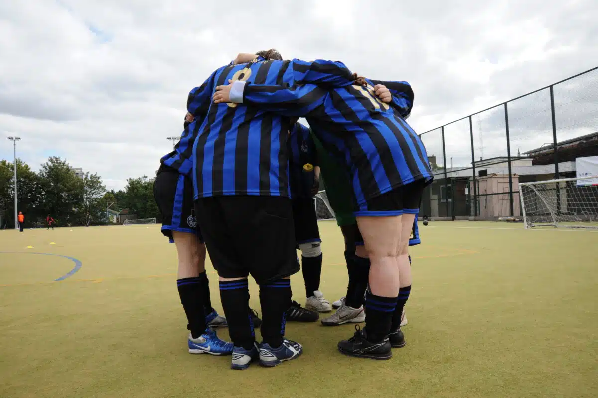 A group of girls in black and blue striped sports shirt huddling together in a circle on a sports pitch. Anonymous imagery taken from a project visit during the 2010 Sport Relief campaign. Taken in London on 9th September 2009. Photo by Rhian Ap Gruffydd/Comic Relief