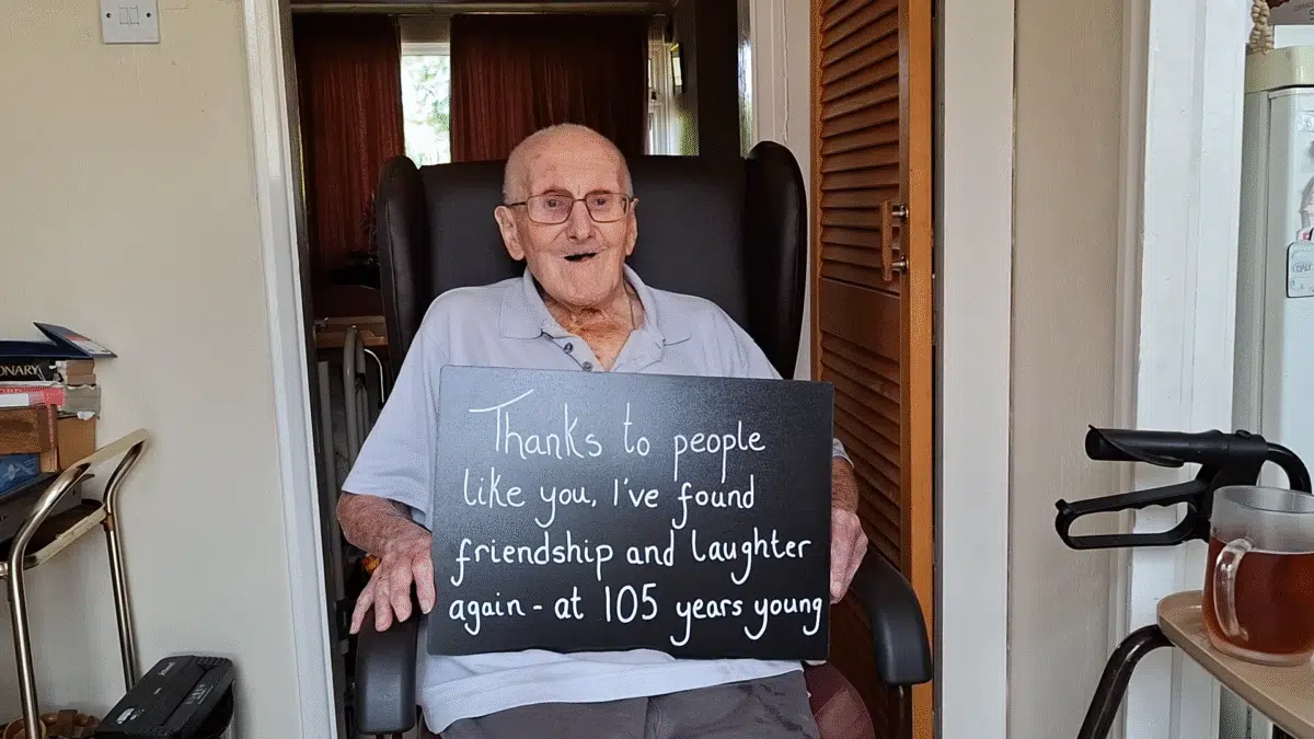 Thanks to people ilke you I've found friendship and laughter again - at 105 years young. A man in a wheelchair holds this message on a black sign.