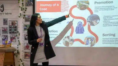 A woman explains the journey of a coat on a displays, as part of Human Appeal's Wrap Up campaign.
