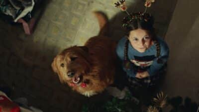 A young girl and her dog look up in a room with Christmas decorations