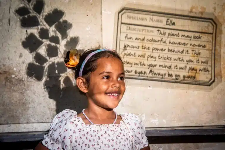 A smiling young girl in front of some writing projected on a screen behind her.
